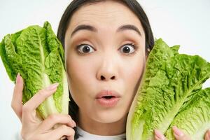 Portrait of cute young woman shows her face with cabbage, likes vegetables, eats healthy nutritious diet food, holds lettuce, white background photo