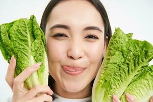 Portrait of cute young woman shows her face with cabbage, likes vegetables, eats healthy nutritious diet food, holds lettuce, white background photo