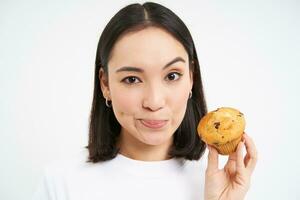 imagen de joven asiático mujer, nutricionista demostración Pastelería magdalena con un montón de calorías, prohibir comiendo basura alimento, blanco antecedentes foto