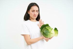 Young woman expresses dislike, rejects eating cabbage, shows no, stop refuse gesture, isolated on white background photo