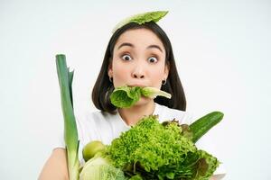 cerca arriba retrato de asiático niña masticando lechuga hoja, participación verde oránico verduras, Guías sano estilo de vida con nutritivo alimento, blanco antecedentes foto