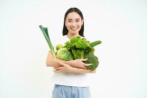Image of smiling asian woman with vegetables, eating healthy green organic food, isolated on white background photo