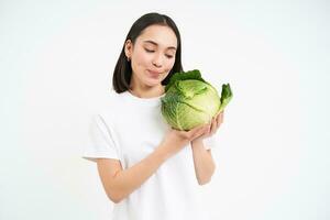 Portrait of lovely korean woman, showing cabbage, holding lettuce green vegetable and smiling, isolated on white background photo