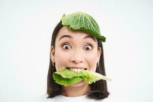 Portrait of cute smiling korean woman with leaf on head, eats cabbage and looks happy, white background photo