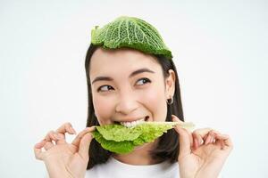 feliz, linda asiático mujer comiendo verde lechuga, vegetariano gustos oránico verduras, blanco estudio antecedentes foto