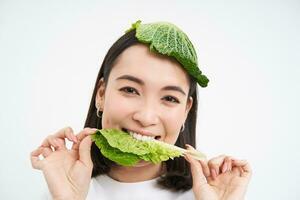 Portrait of asian girl with leaf on head, eats cabbage and smiles, isolated on white background photo