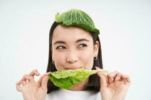 Portrait of asian girl with leaf on head, eats cabbage and smiles, isolated on white background photo