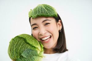 cerca arriba retrato de sano sonriente asiático mujer, demostración repollo, verde letura, con hoja en cabeza, aislado en blanco antecedentes foto