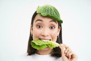 retrato de linda sonriente coreano mujer con hoja en cabeza, come repollo y mira feliz, blanco antecedentes foto