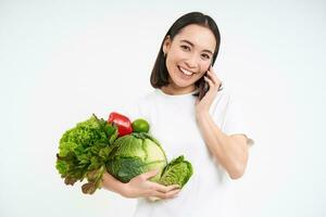 Happy healthy woman, calls merchant, orders organic vegetables and smiles, white background photo