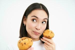 Pensive smiling young woman holding cupcake and thinnking photo