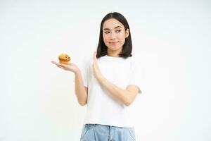 Cute asian girl with will power, refuses the cupcake, stays on diet, isolated on white background photo