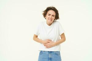 Image of woman with stomach ache, touching her belly, grimacing from pain or discomfort, has painful menstrual cramps, isolated over white background photo