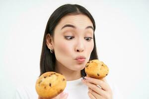 Close up portrait of asian girl eats cupcakes with happy face, isolated on white background photo