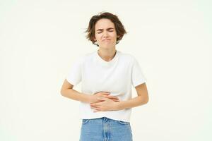 Image of woman with stomach ache, touching her belly, grimacing from pain or discomfort, has painful menstrual cramps, isolated over white background photo
