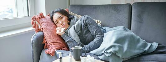 Sick woman lying on sofa at home, catching cold. Young girl freezing from heating problem in her apartment, concept of high cost of living photo