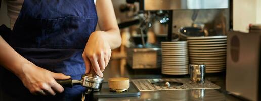 Close up of barista female hands pressing coffee into tamper, prepares order in cafe behind counter photo