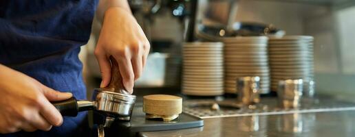 cerca arriba de barista hembra manos prensado café dentro manosear, prepara orden en café detrás mostrador foto