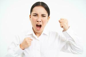 Angry asian woman yells and shakes fists, shouts at employees, stands frustrated against white background photo