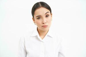 Portrait of skeptical asian woman, looks unamused and serious at camera, stands isolated on white background photo