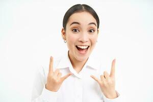 Excited corporate woman, office lady shows rock n roll, heavy metal gesture, has fun, stands over white background photo