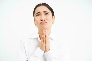 Upset asian woman looks up with desperate and sad face, complains to Lord, stands over white background photo