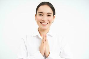 namasté. sonriente japonés mujer muestra manos en orar, dice gracias tú, arcos cortésmente, soportes terminado blanco antecedentes foto