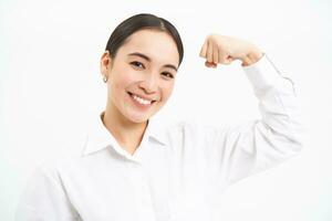 Portrait of confident and strong businesswoman, flexing biceps, shows strength, muscles, stands over white background photo