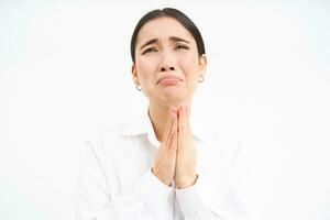 Upset asian woman looks up with desperate and sad face, complains to Lord, stands over white background photo