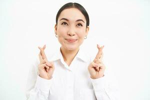 japonés mujer de negocios cruzar dedos para bueno suerte, hace desear, tiene alto esperanzas, anticipa algo, soportes terminado blanco antecedentes foto