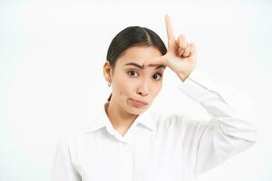 Failure. Close up portrait of korean business woman shows L letter, loser word on forehead, stands over white background photo