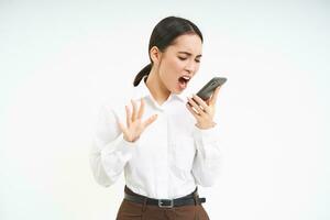 Angry business woman shouts at mobile phone, has intense conversation on telephone, stands over white background photo