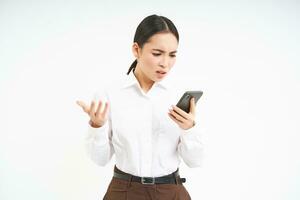 Korean businesswoman looks confused and frustrated at smartphone screen, reads strange message on her phone with puzzled face, shrugs shoulders photo