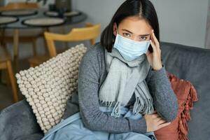 Woman in medical face mask has covid-19, stays at home in personal protective equipment, catching flu, sitting in living room photo