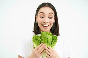 Vegetarian nutrition. Smiling happy young woman looks at her self grown cabbage, eating lettuce, white background photo