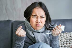 Cost of living and heating problems. Close up of angry girl sneezing, staying at home and freezing, wearing warm clothes and scarf photo