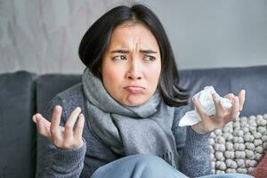 Cost of living and heating problems. Close up of angry girl sneezing, staying at home and freezing, wearing warm clothes and scarf photo