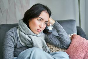 Portrait of sad woman feeling unwell, wearing warm clothes and scarf at her home without heating, staying on sick leave in her house photo