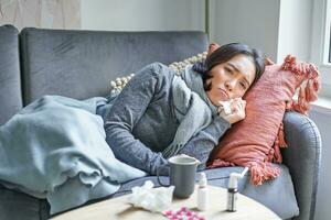 Sick woman lying on sofa at home, catching cold. Young girl freezing from heating problem in her apartment, concept of high cost of living photo