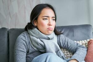 Portrait of sad woman feeling unwell, wearing warm clothes and scarf at her home without heating, staying on sick leave in her house photo