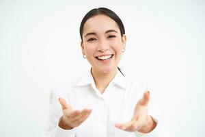 Portrait of asian businesswoman welcomes you, corporate worker invites you, extends hands and smiles friendly, stands over white background photo