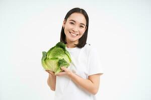 Beautiful korean woman, holding cabbage and smiling, isolated on white studio background photo