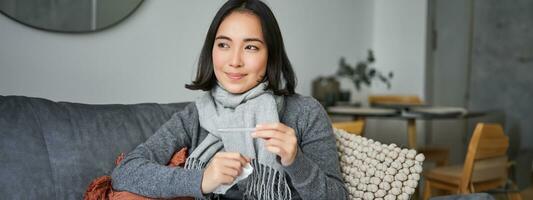 Smiling asian woman holding thermometer and looking pleased, feeling better after cold, got rid of fever, has normal temperature photo