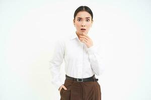 Asian saleswoman with shocked face, opens mouth and stares at camera, stands over white background photo