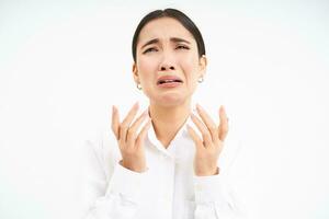 Upset asian woman looks up with desperate and sad face, complains to Lord, stands over white background photo