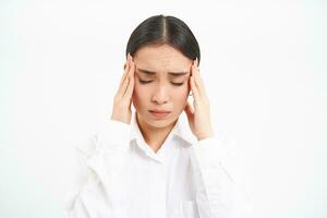 Tired woman, office worker holds hands on head, migraine or headache, looks upset and troubled, stands over white background photo