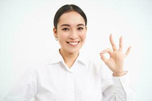 Confident saleswoman, team leader shows okay, ok sign in approval, say yes, recommends something, stands over white background photo
