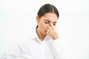 Tired saleswoman, young asian woman in office, massages her eyes, has fatigue after work, isolated on white background photo