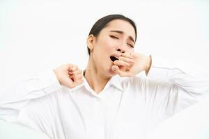 Tired businesswoman, korean entrepreneur yawns, feels tired, covers opened mouth with hand, stands isolated on white background photo