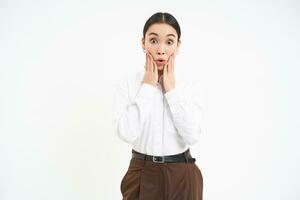 Corporate woman looks amazed, holds hands near face with surprised face expression, isolated on white background photo